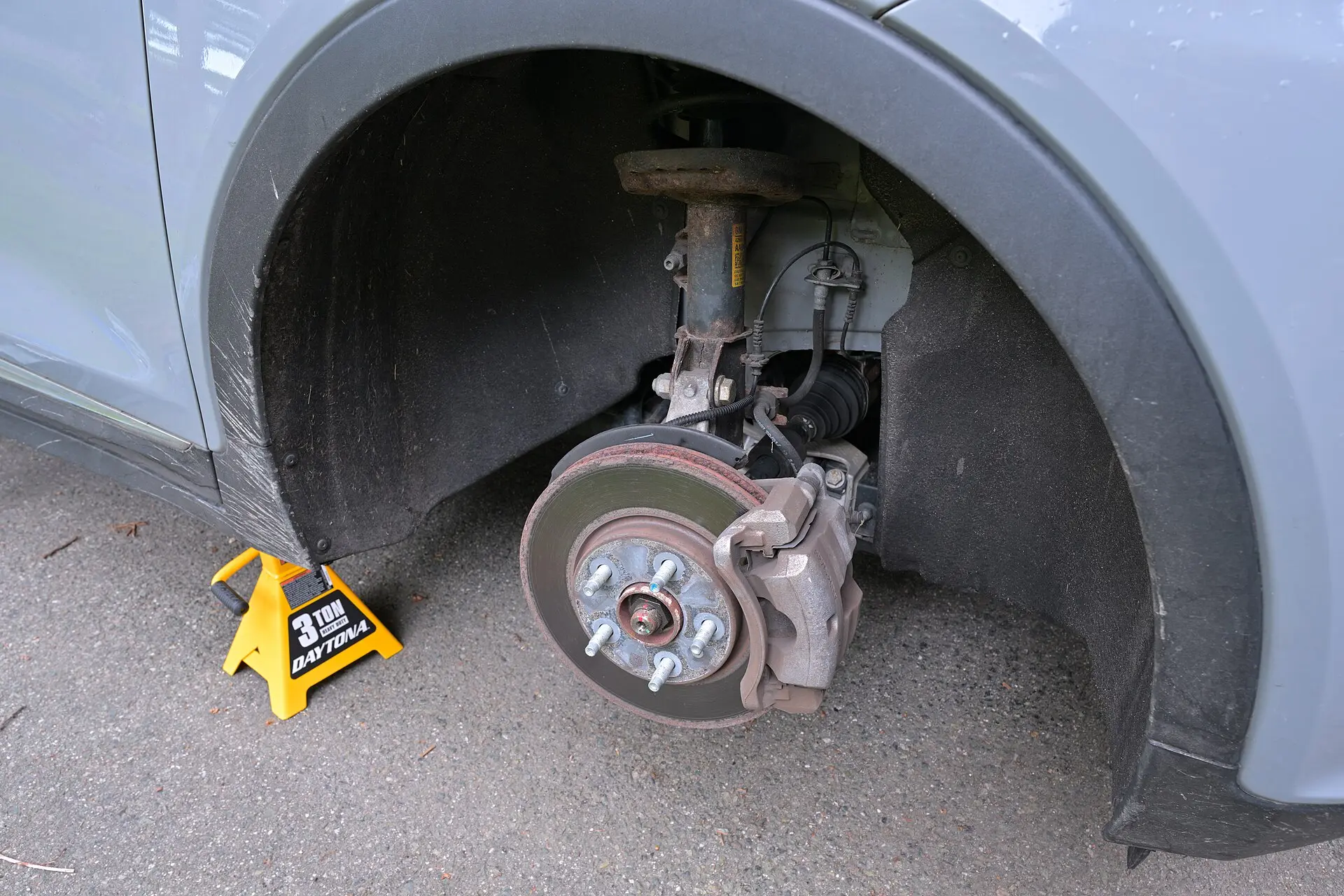 A car on a jack with the front wheel off, showing the brake disc and suspension
