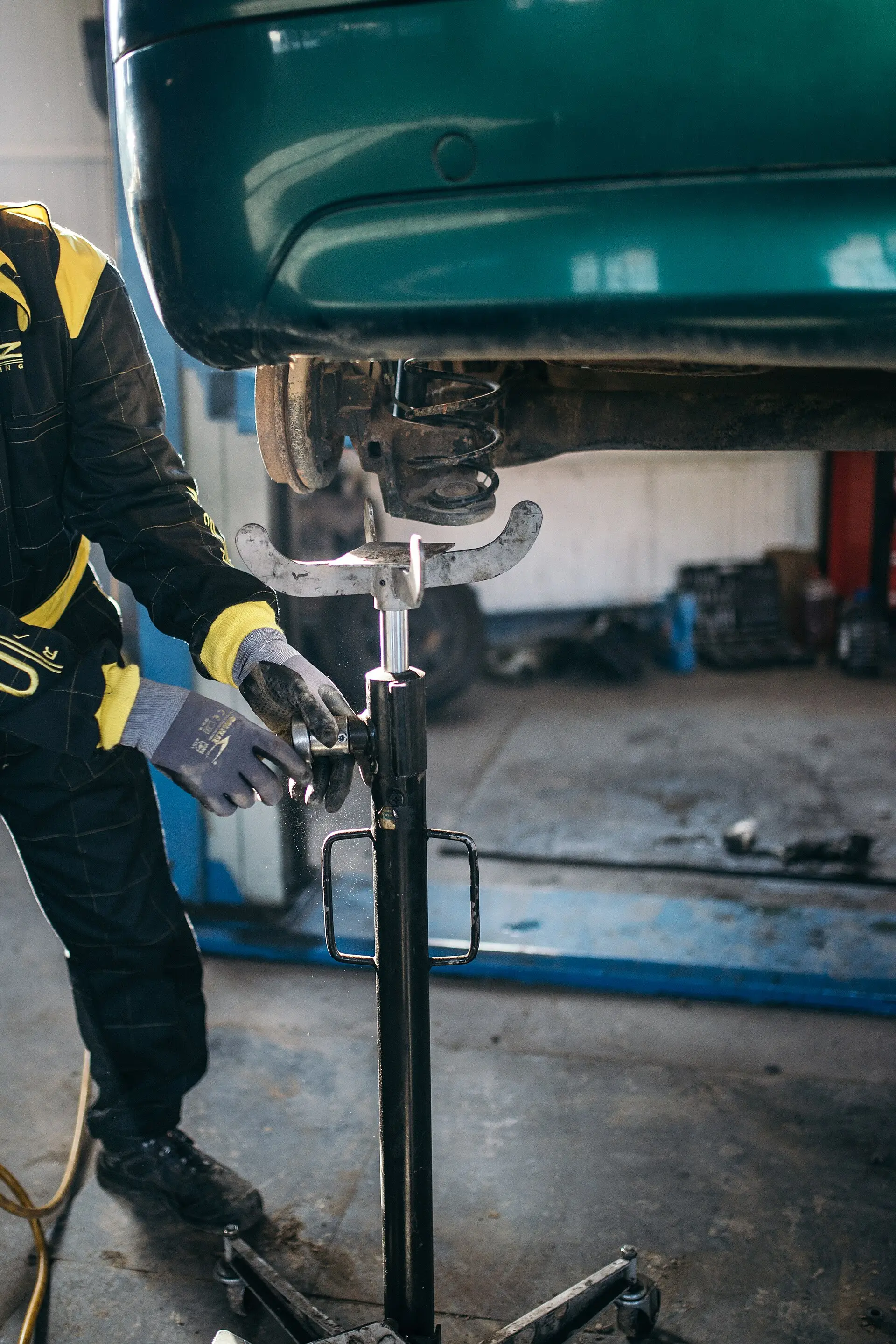 A mechanic in gloves works on the suspension of a car raised on a lift