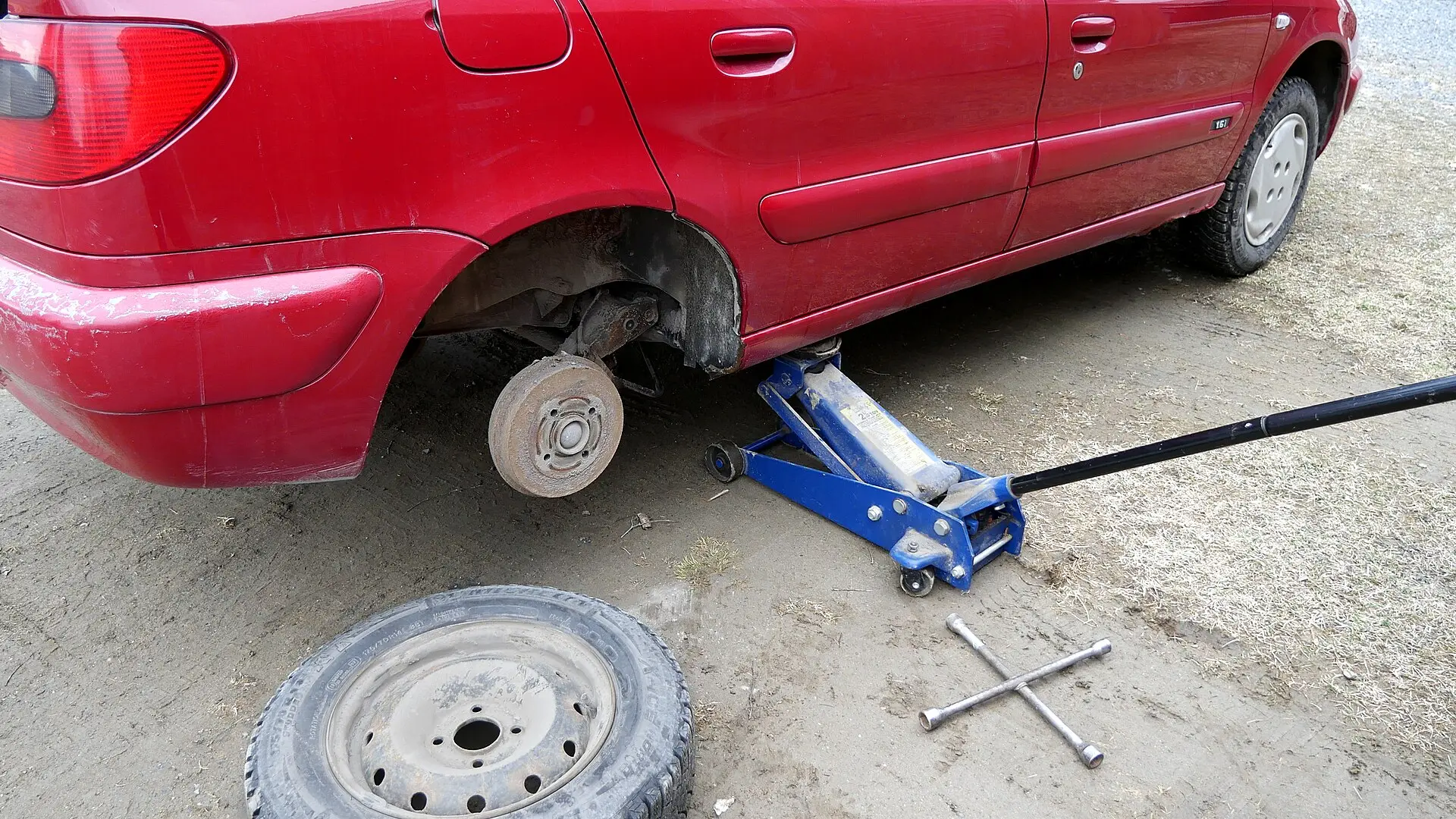 A car raised on a jack with a wheel removed beside a spare tire